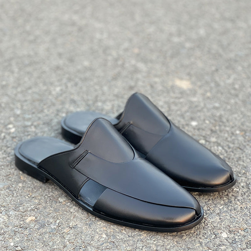 Pair of handmade black leather mules for men on a grey asphalt surface