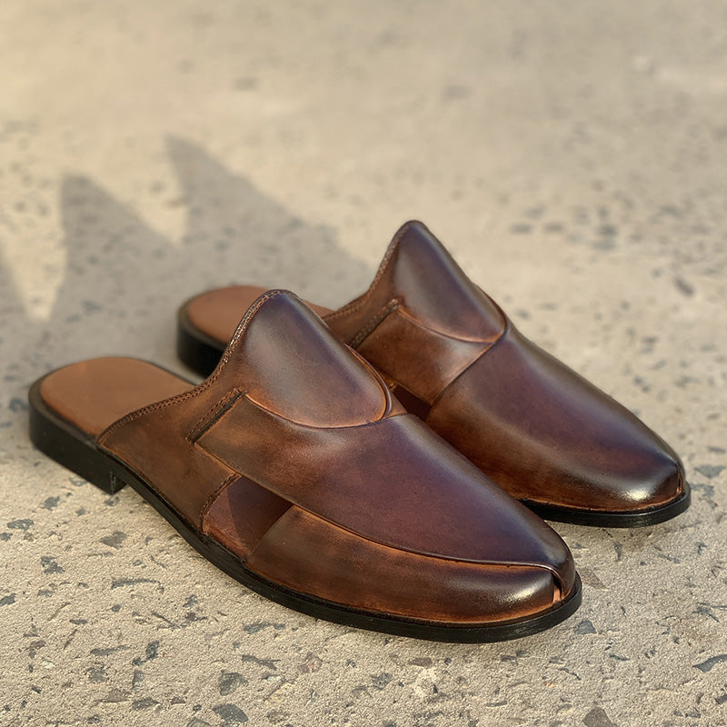Handmade brown leather mules for men on a concrete surface