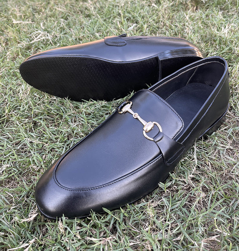 Pair of handmade black leather men's loafers with gold horsebit detail on green grass