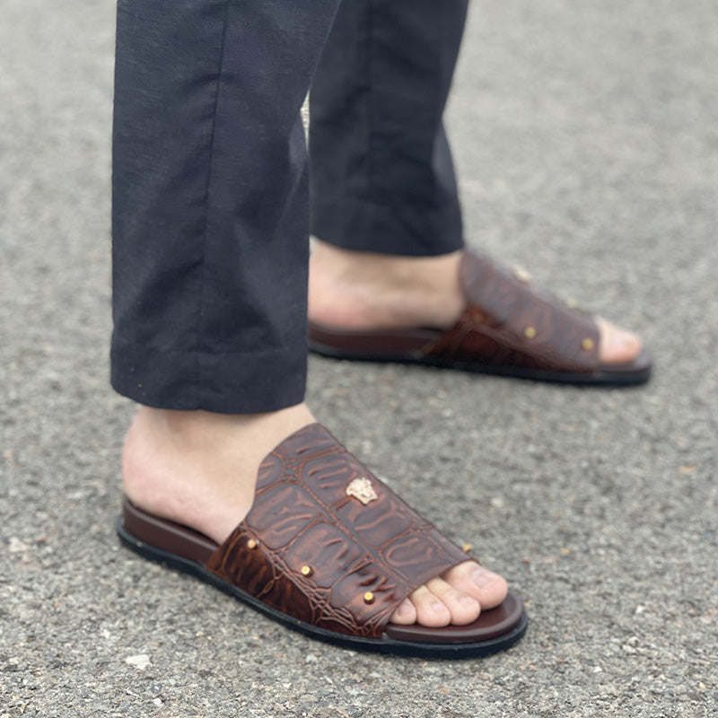 Close-up of men's brown croc-embossed leather slides with gold stud details.