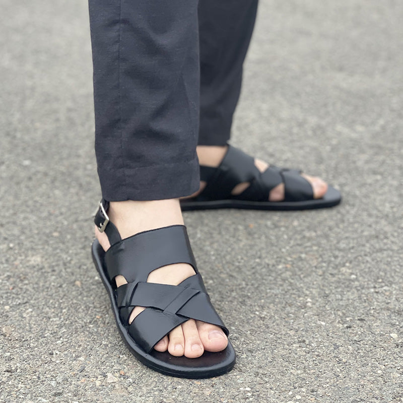 Close-up of a man wearing black leather handmade sandals with a strap buckle