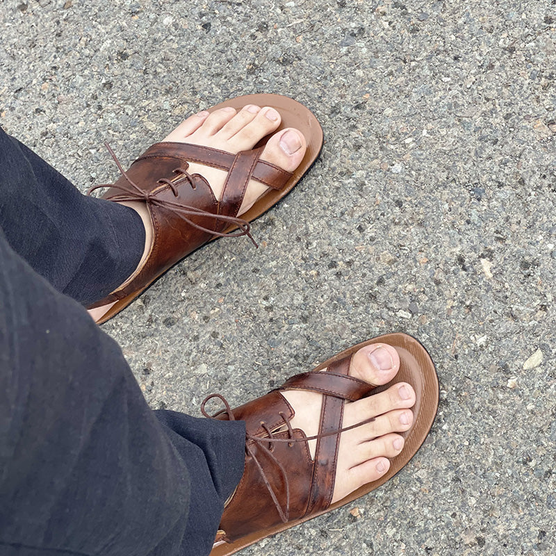 Handmade brown leather strappy sandals for men on a grey pavement surface