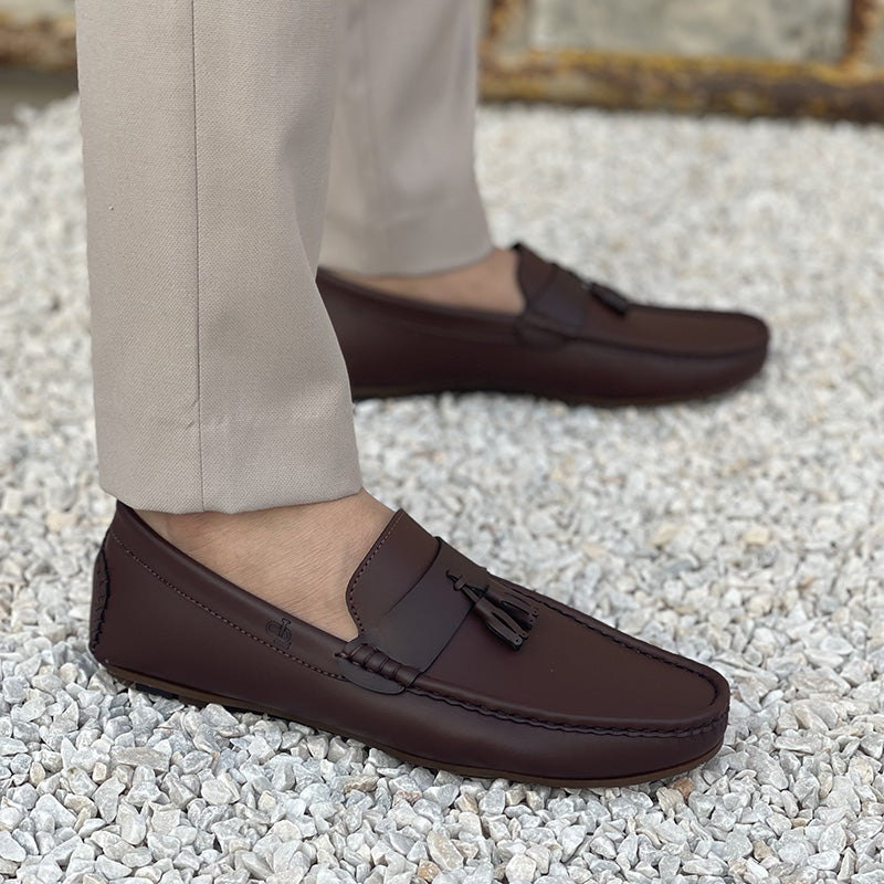 Man wearing dark brown leather tassel loafers with beige trousers on white pebbles