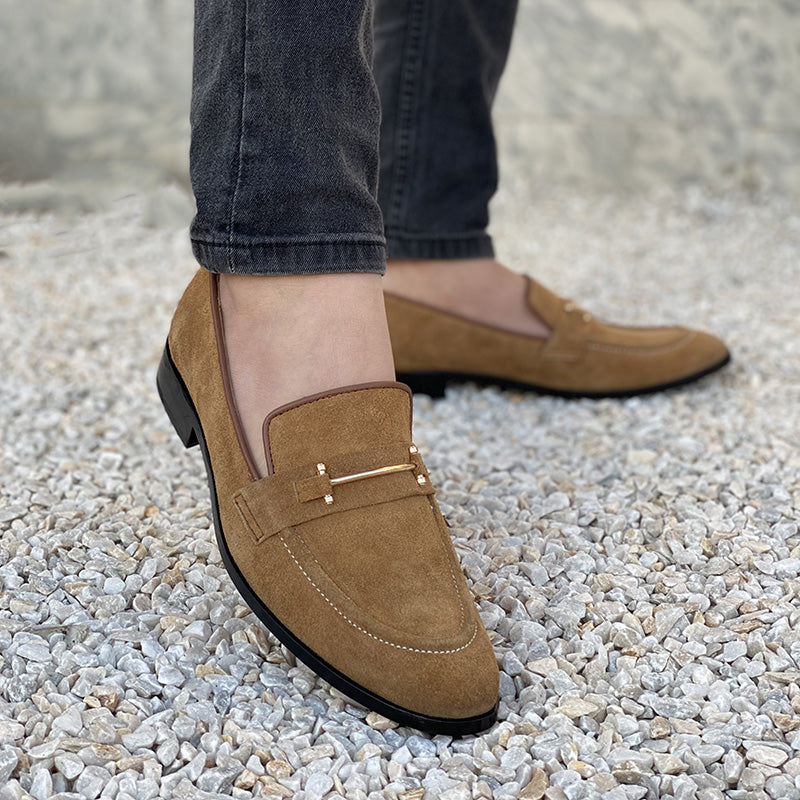 Man wearing brown suede loafers with gold metal detail on a gravel surface