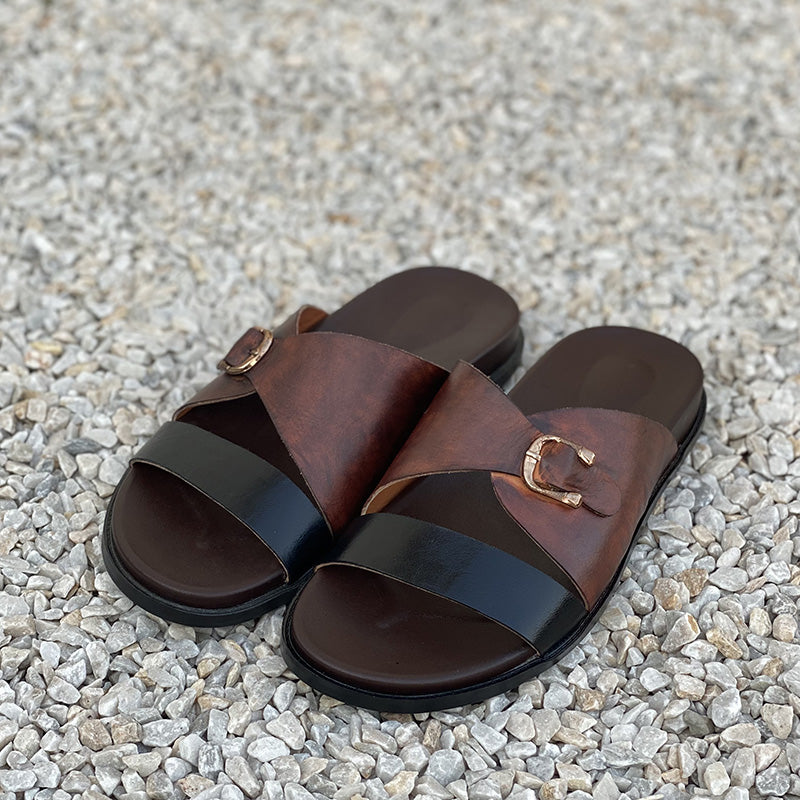 Handmade brown and black leather cross-strap sandals for men on a pebble surface