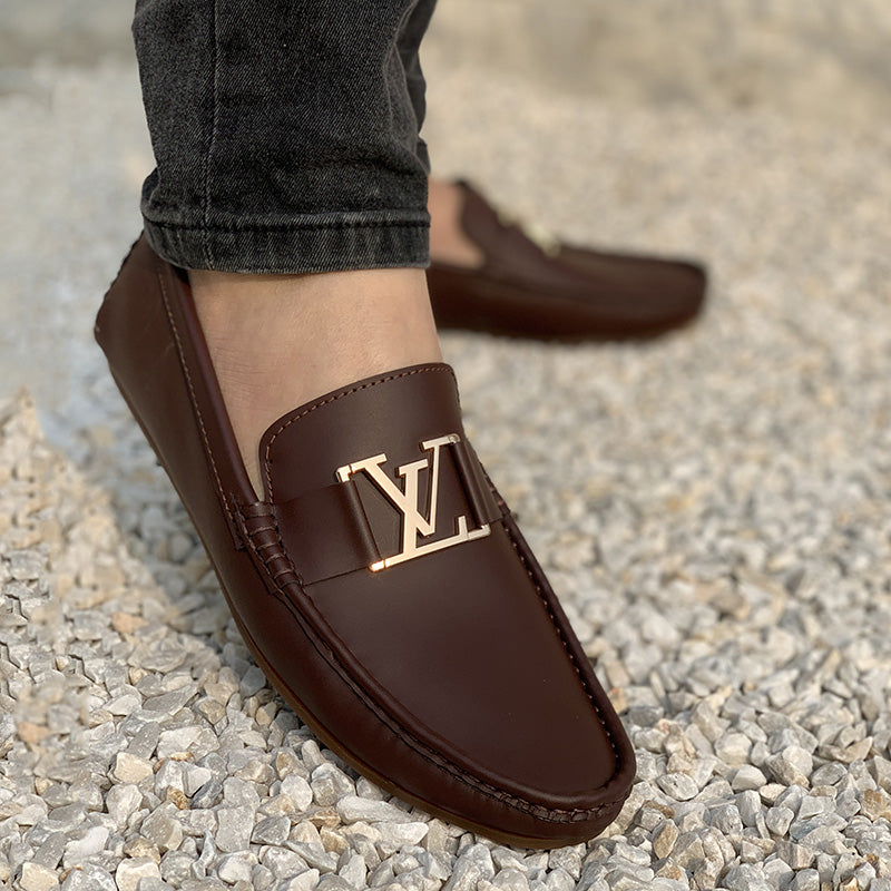 Brown leather men's loafers with gold LV buckle on a gravel surface