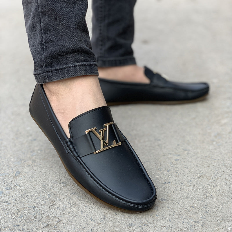 Man wearing black leather loafers with a gold buckle detail and grey jeans