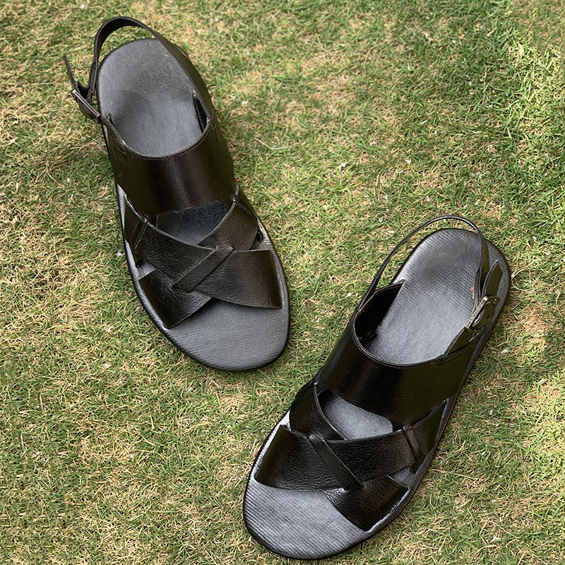 Pair of handmade black leather criss-cross strap sandals for men on green grass