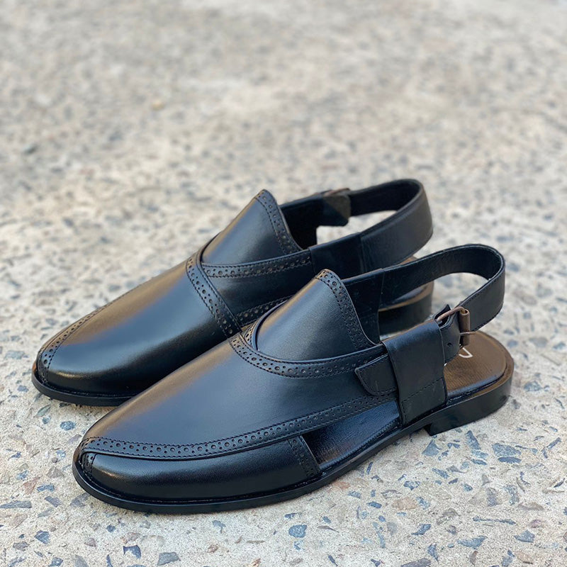 Pair of handmade black leather men's sandals with perforated detailing on a stone surface