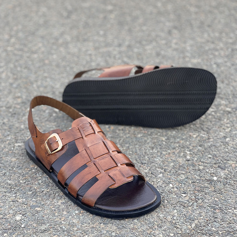Handmade brown leather strappy sandals for men on a gray paved surface