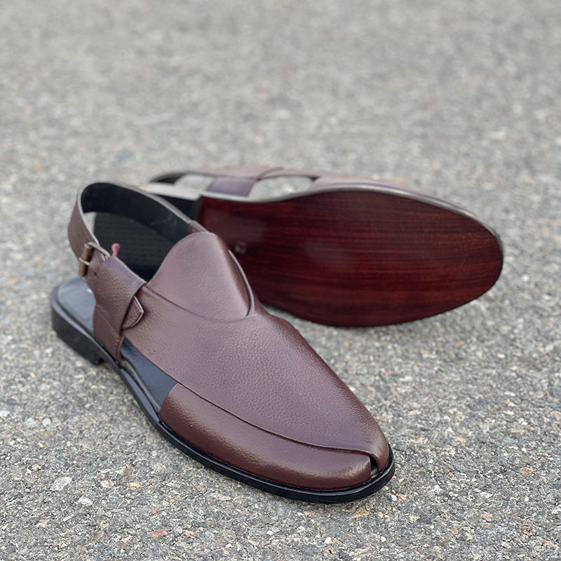 Handmade brown leather men's mules with a pointed toe and strap closure on asphalt.