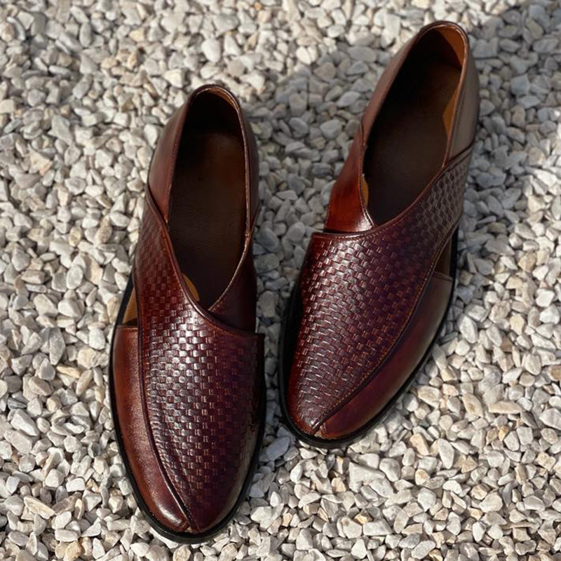 Pair of handmade brown woven leather men's loafers on a grey pebble background
