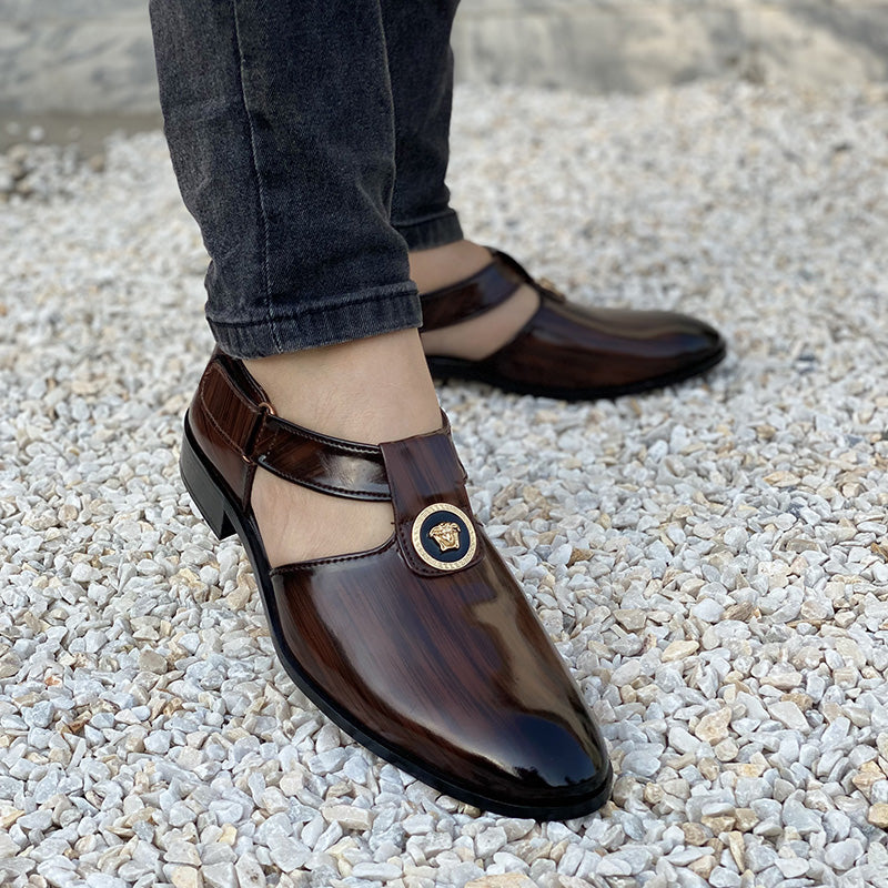 Men's brown polished leather formal shoes with gold medallion detail on white pebbles