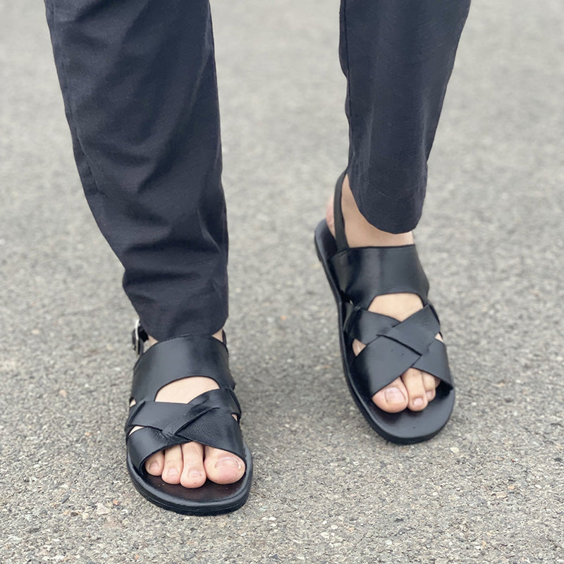 Man wearing handmade black leather criss-cross strap sandals with black trousers.