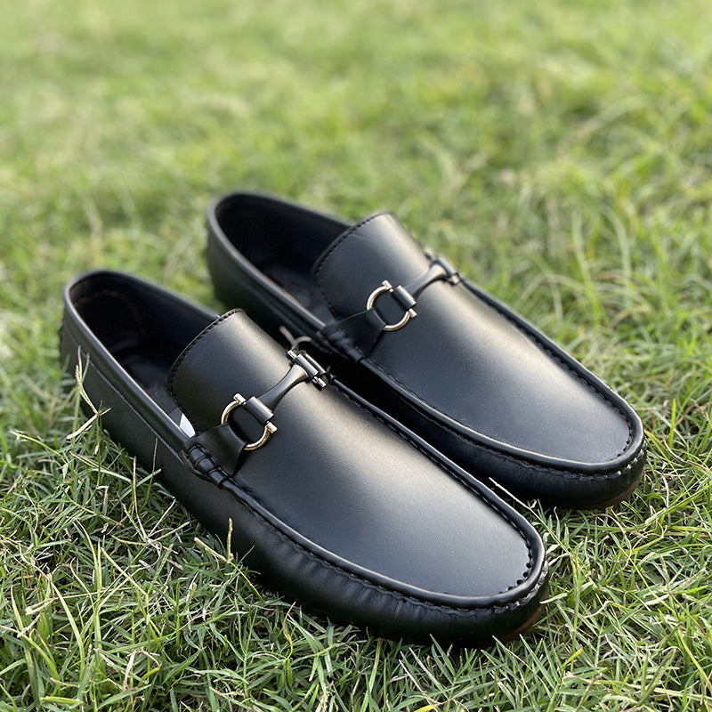 Black leather men's loafers with gold horsebit detail on green grass