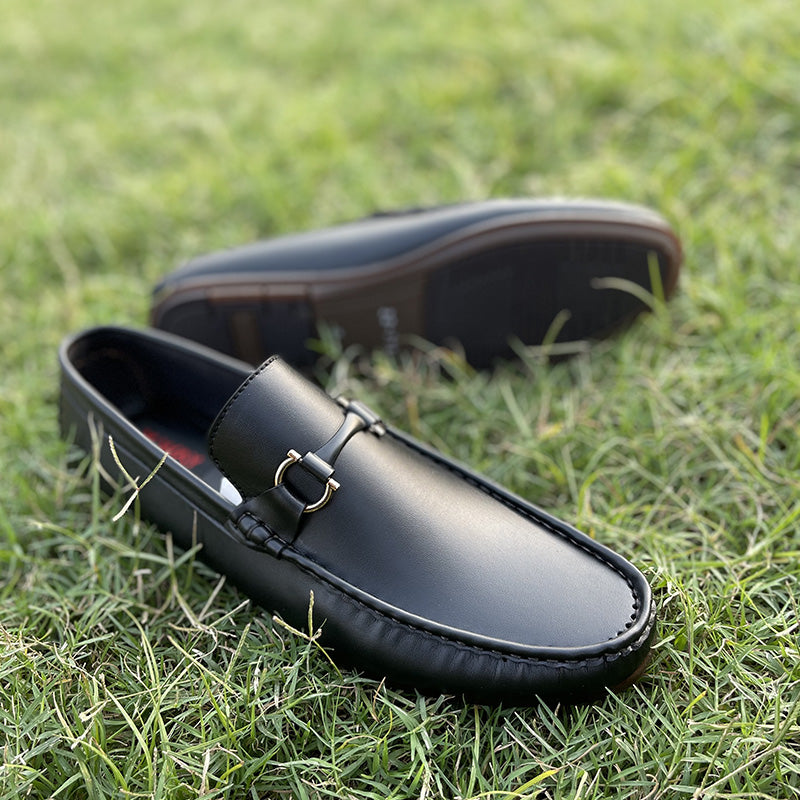 Black leather men's loafers with gold bit detail on green grass.