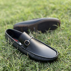 Black leather men's loafers with gold bit detail on green grass.