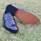 Black crocodile pattern men's leather loafers on green grass.