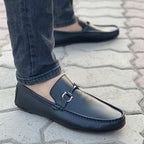 Black leather men's loafers with gold metal hardware worn with denim jeans.