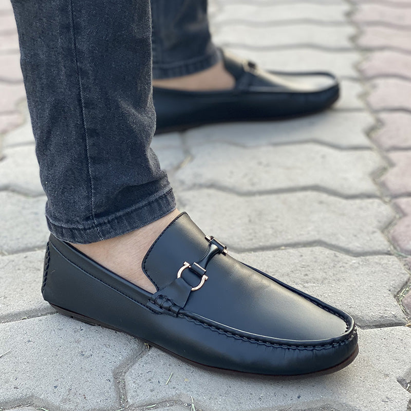 Black leather men's loafers with gold metal hardware worn with denim jeans.