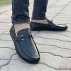 Men's black leather loafers with gold bit detail worn with denim jeans.