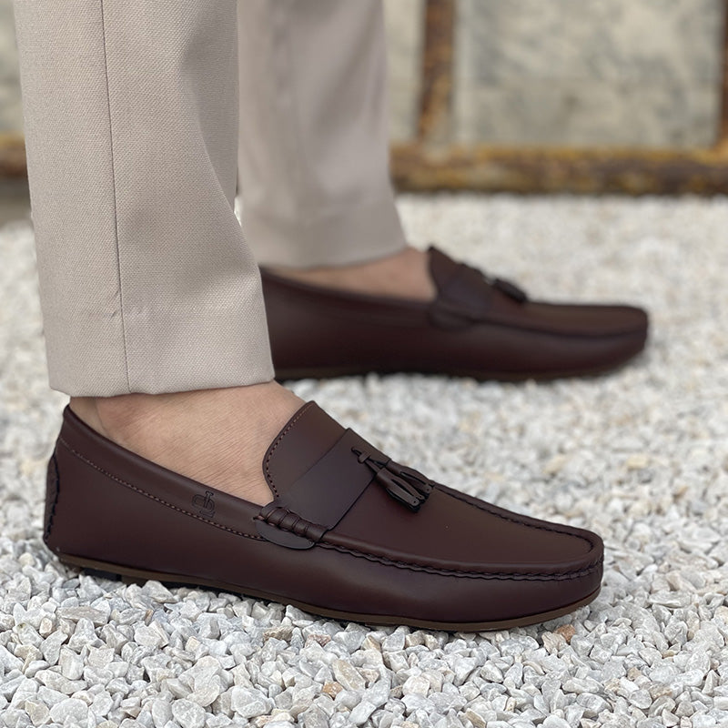 Close-up of men's brown leather tassel loafers worn with beige trousers on a gravel surface