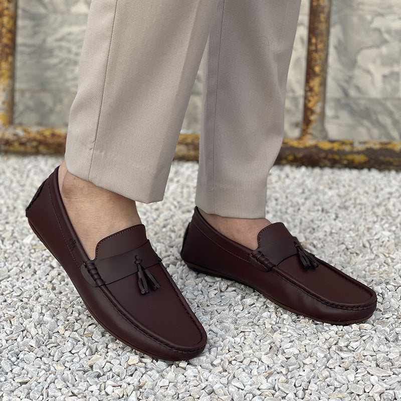 Close-up of men's dark brown leather tassel loafers worn with beige trousers.