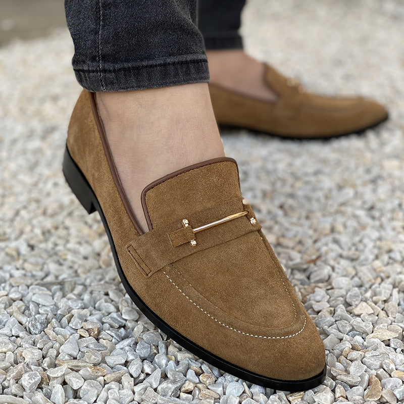 Men's brown suede loafers with gold hardware on a pebble background