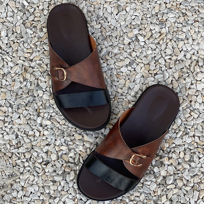 Pair of handmade brown and black leather criss-cross strap sandals for men on white pebbles.