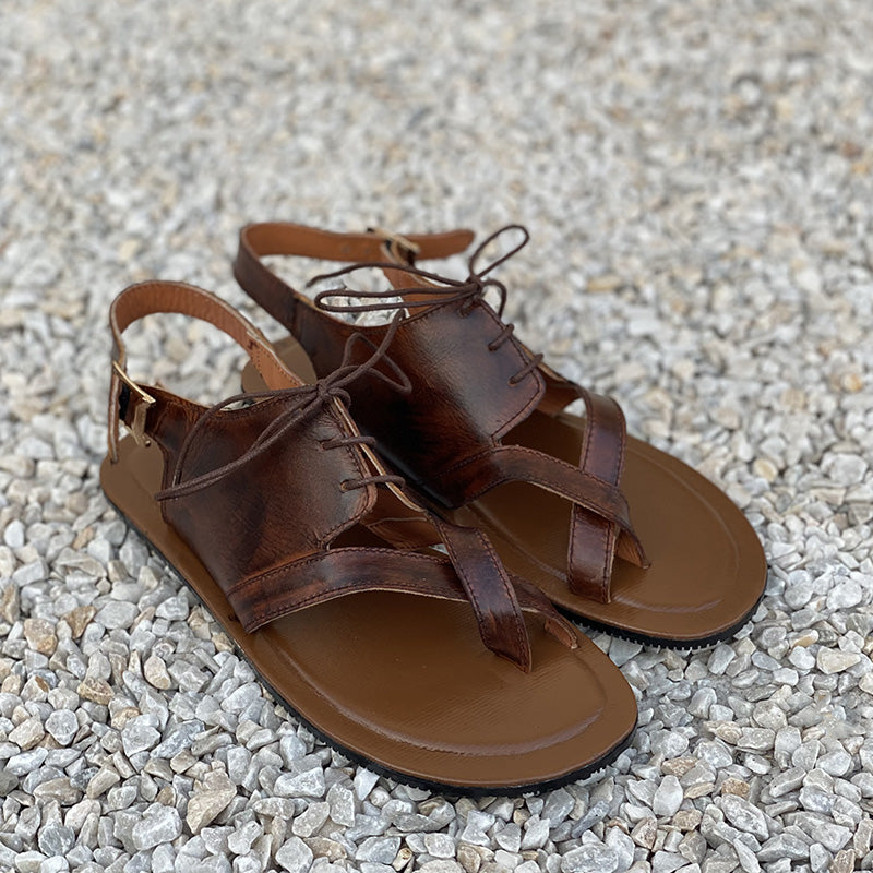 Handmade brown leather men's sandals with strap detailing on a pebble background
