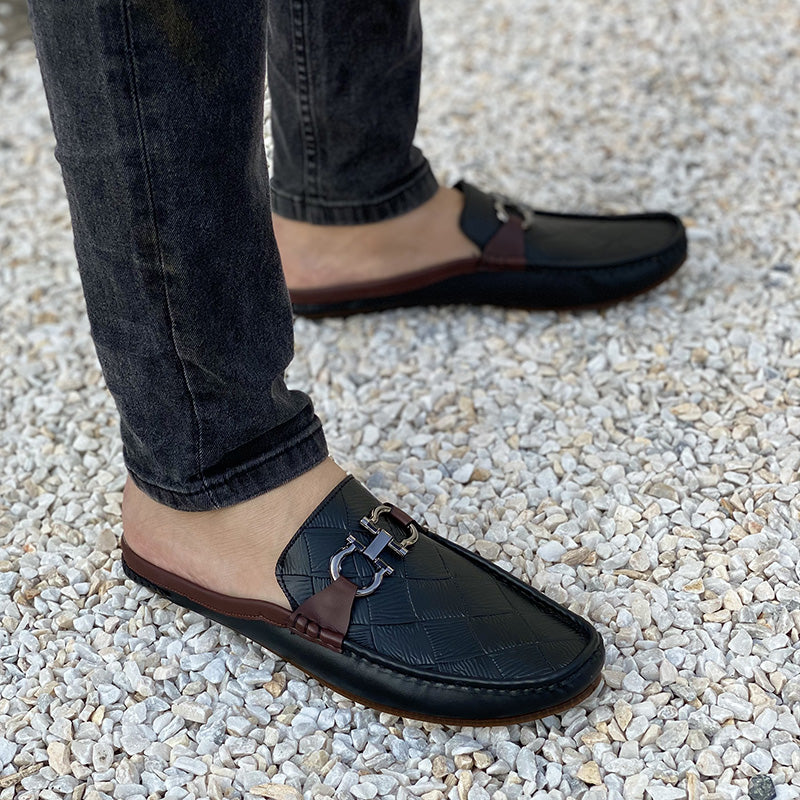 Man wearing black handmade leather mule loafers with metal bit detail and brown sole.