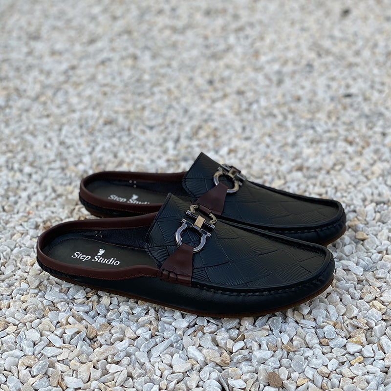 Pair of black handmade leather mules for men with metallic buckle detail on pebble background
