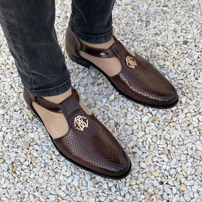 Man wearing brown snakeskin textured handmade formal shoes with gold emblem on gravel