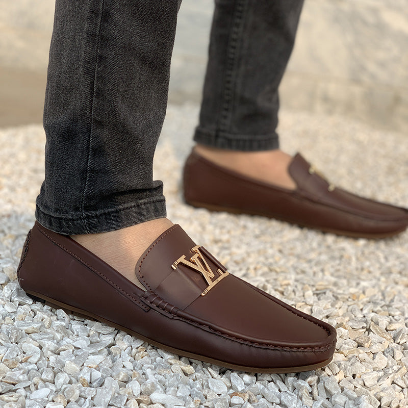 Man wearing brown leather loafers with a gold buckle on a gravel surface