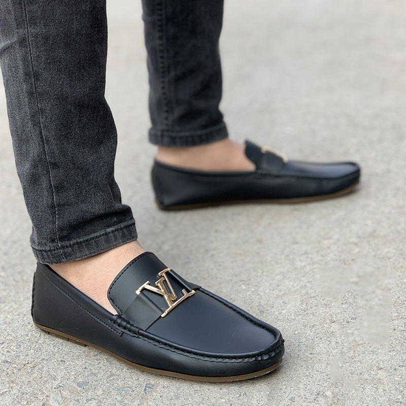 Man wearing black leather loafers with gold buckle detailing and dark grey jeans.
