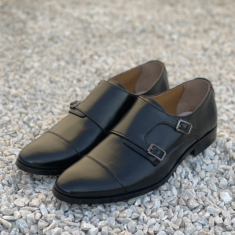 Pair of handmade black leather double monk strap formal shoes on a gravel background