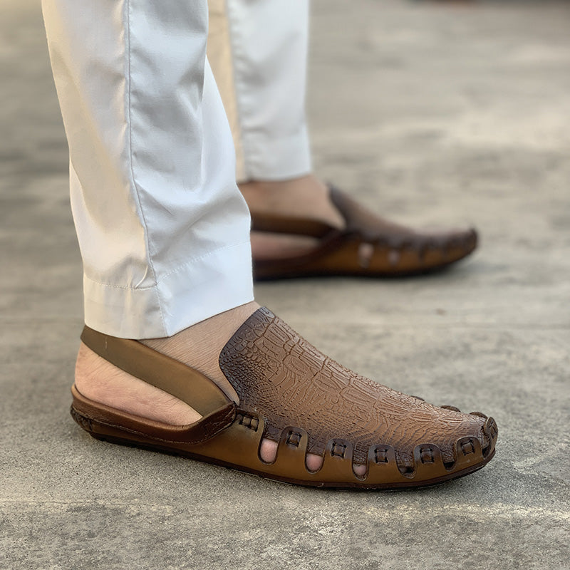 Close-up of brown textured leather Peshawari Chappal sandals worn with white trousers.