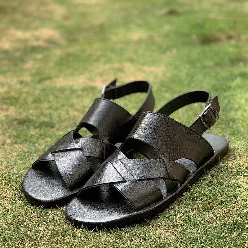 Pair of handmade black leather sandals for men on a green grass background