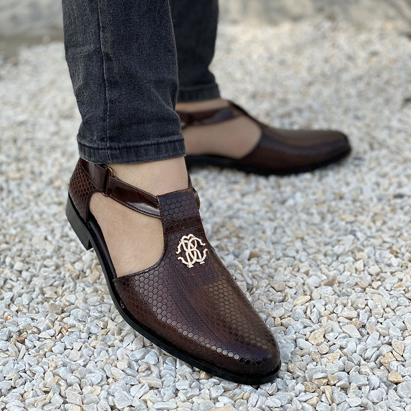 Close-up of brown textured leather handmade men's loafers with gold monogram on white pebbles