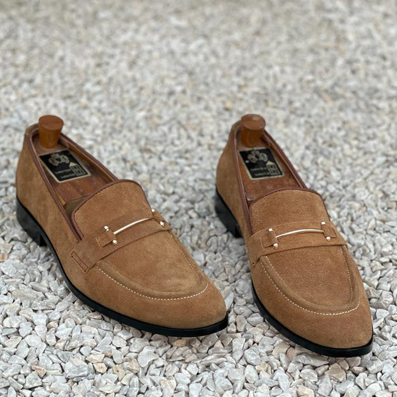 Pair of men's brown suede loafers with gold metal hardware on a white pebble background
