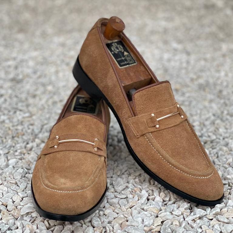 Pair of brown suede handmade loafers for men with gold-tone metal hardware on a stone background
