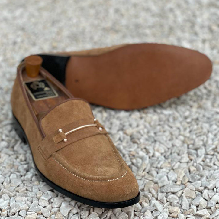 Handmade brown suede loafers for men with gold hardware on a pebble background