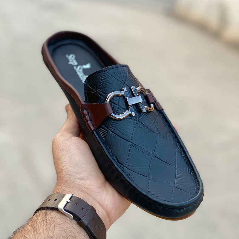 Hand holding a black quilted leather mule shoe with a silver buckle and brown accents.