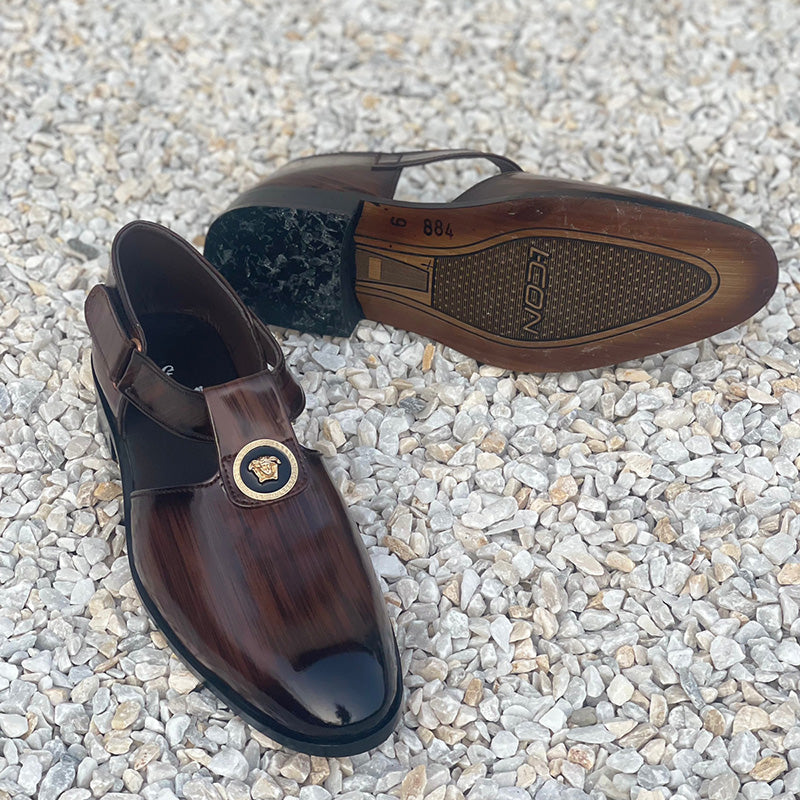Handmade brown leather men's formal shoes with gold emblem on a white pebble surface